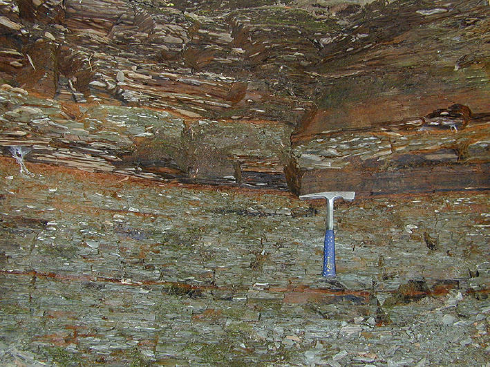 A photograph shows a large rock outcrop with different horizontal layers of shale, with a street light on the right and a road at the bottom.