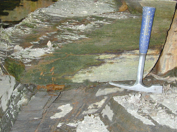 A photograph of a rock outcrop shows a geologic hammer resting on a green-tinted rock surface, with a small stream of water dripping down the rock face.