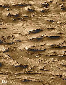 Aerial view of layered, wind-eroded rock formations on Mars, showing ridges and striations. Scale bar indicates 100 meters